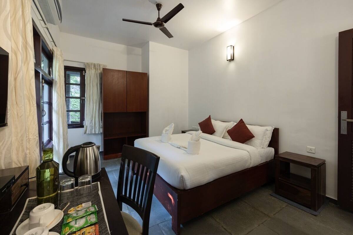 Een keurig opgeruimde hotelkamer met een bed, een bureau met stoel, een koffiezetapparaat en een plafondventilator.