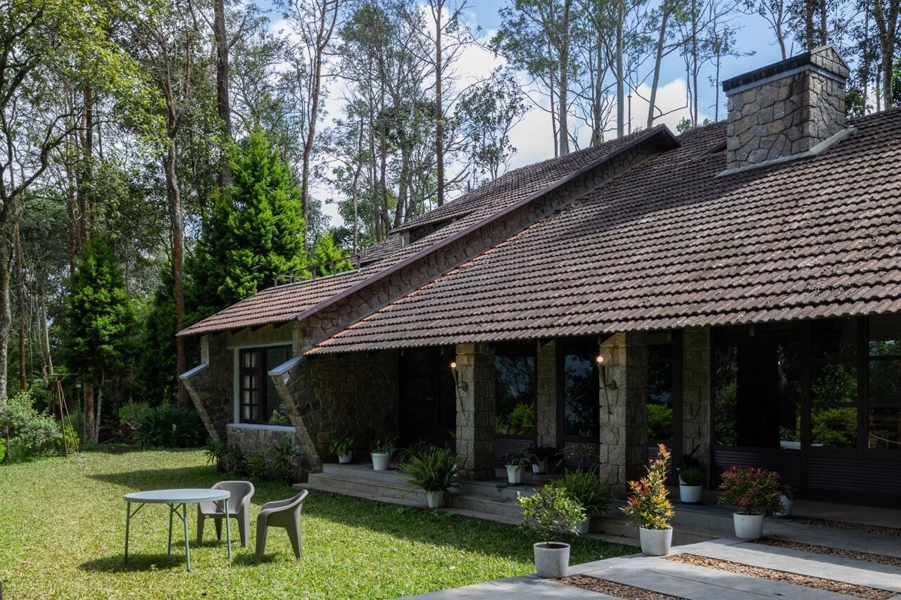 Une maison en pierre avec un toit de tuiles, entourée d’une cour verdoyante et d’arbres.