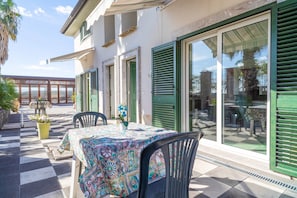 Un patio con mesa y sillas, una planta en maceta y vistas al mar a través de amplios ventanales.