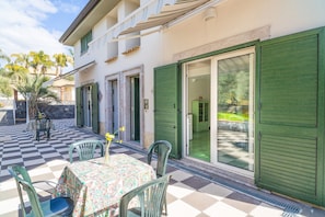 A patio with a checkered floor, a table with a patterned tablecloth, and green chairs.
