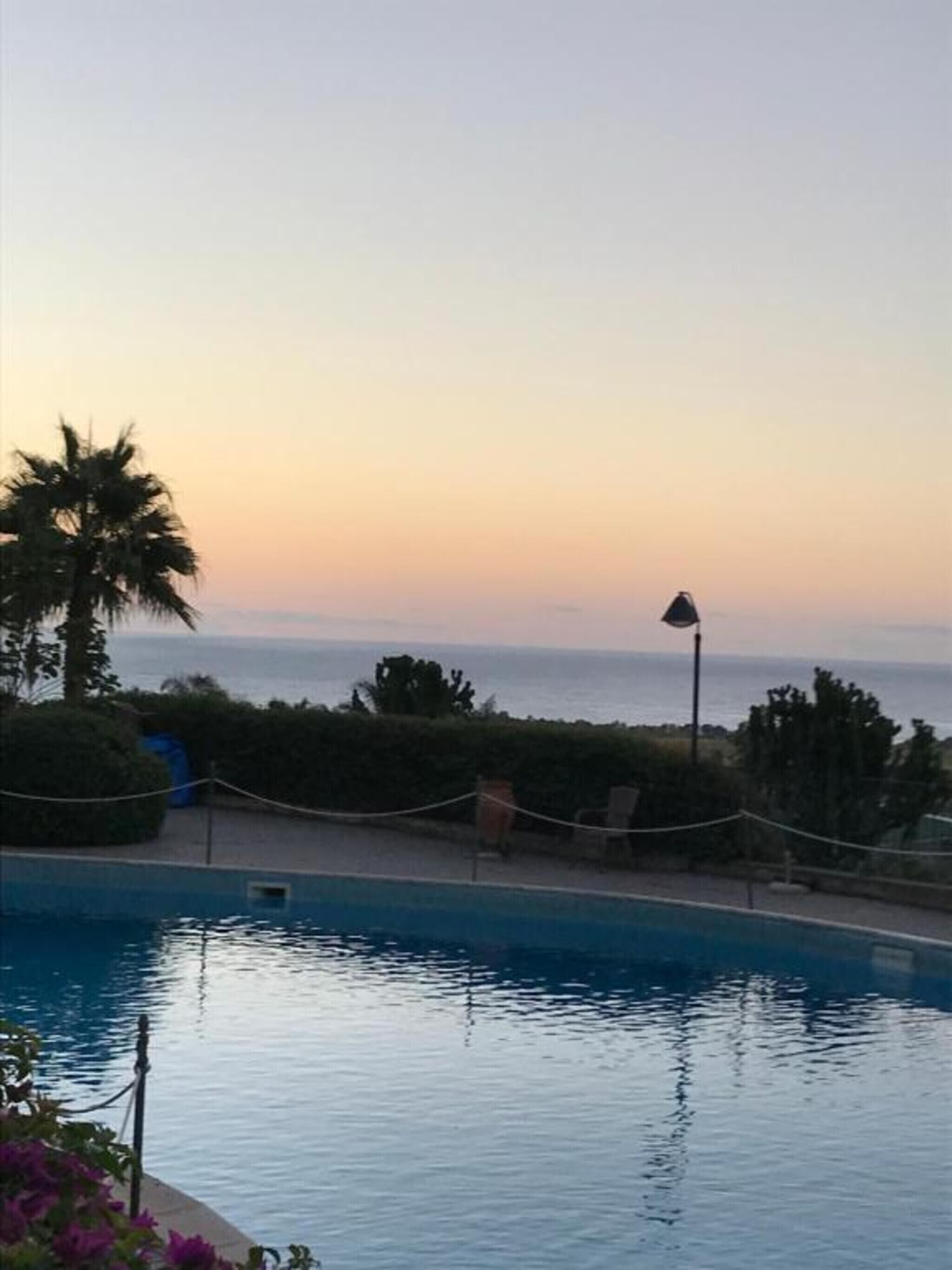 A swimming pool with a view of the ocean at sunset.