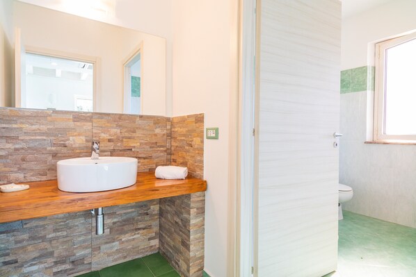Un baño con pared de piedra, encimera de madera, lavabo blanco y retrete.