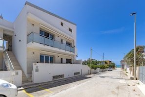A modern two-story building with a balcony, a staircase, and a view of the sea.