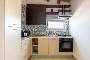 A compact kitchen with a stove, sink, and dishwasher, featuring light wood cabinets and a tiled backsplash.