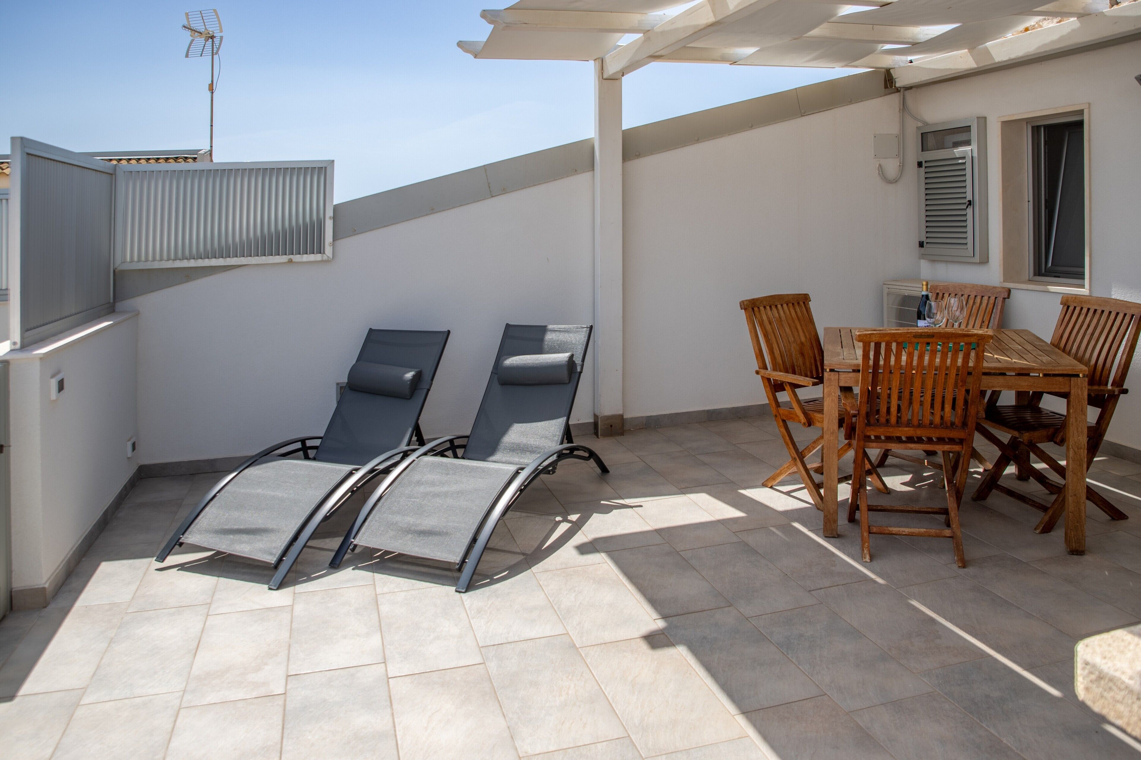 Een terras op het dak, met een tafel, stoelen, een pergola en een tv-antenne.