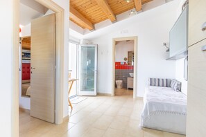Ein geräumiges Zimmer mit einem Bett, einer Holzbalkendecke, einem Badezimmer mit Toilette und Waschbecken sowie einer roten Wand.