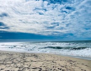 Een strand met voetafdrukken die naar het water leiden, golven die op de kust breken en een gedeeltelijk bewolkte lucht.