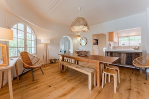 Een ruime keuken met houten vloeren, een grote eettafel en rieten stoelen.