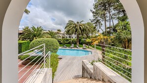 A pool area with a wooden deck, a white railing, and a view of a building with a tiled roof.