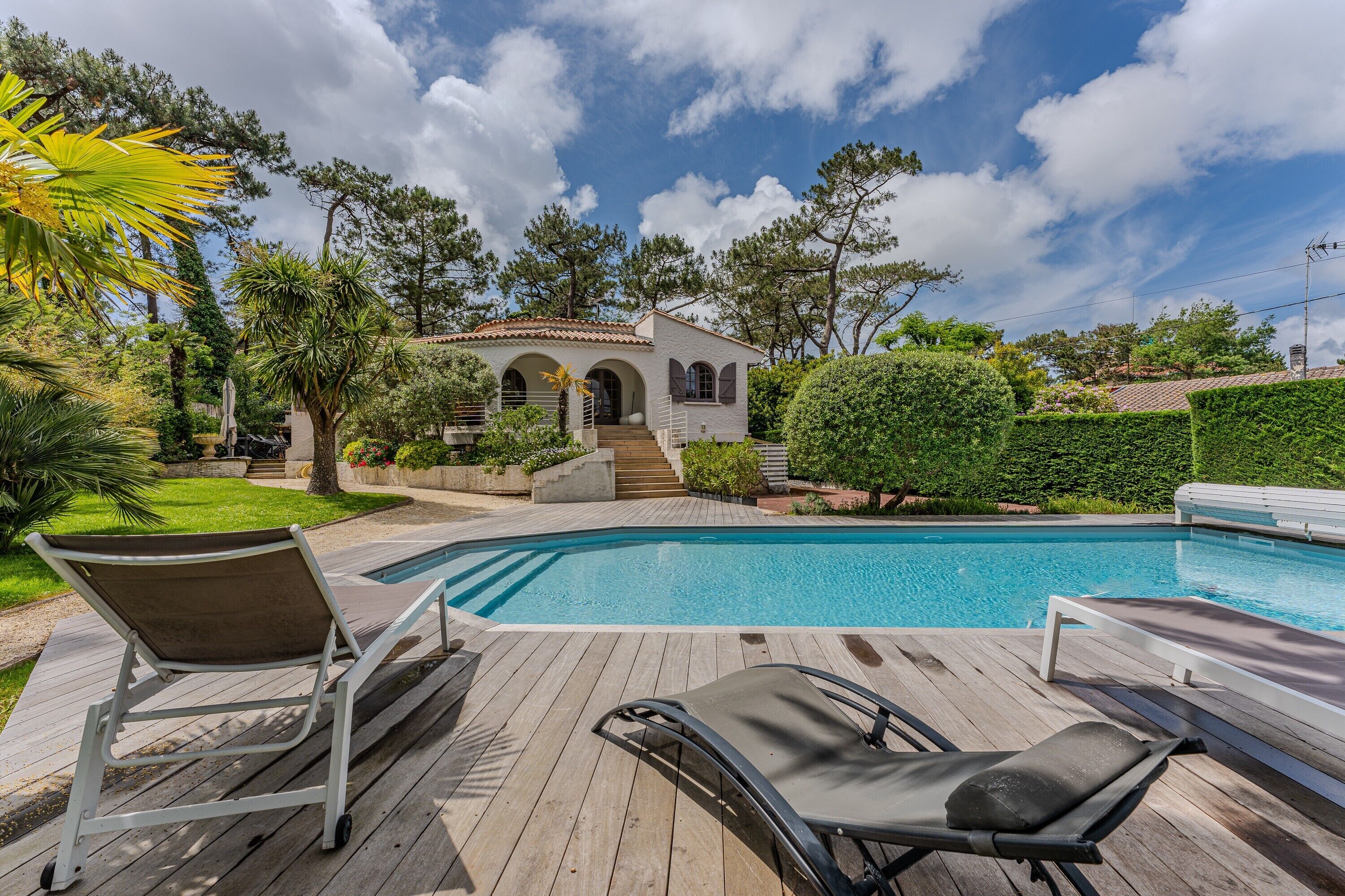 A pool with lounge chairs, a small building with arched windows, and a well-maintained garden.