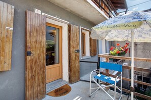 Une porte en bois avec un numéro, une chaise bleue, une petite table ornée d’un arrangement floral et un paillasson sur lequel est écrit « HOME HOME ».
