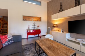 A modern living room with a wooden coffee table, a grey sofa, a red dresser, and a flat-screen TV mounted on the wall.