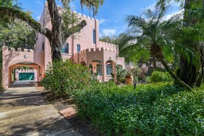A castle-like building with a pink facade, arched windows, and a large tree in the foreground. - Historic Home, Perfect for Special Occasions, 3 Master Suites, Steps to Sites, $300 in Free Tickets! (St. Augustine)
