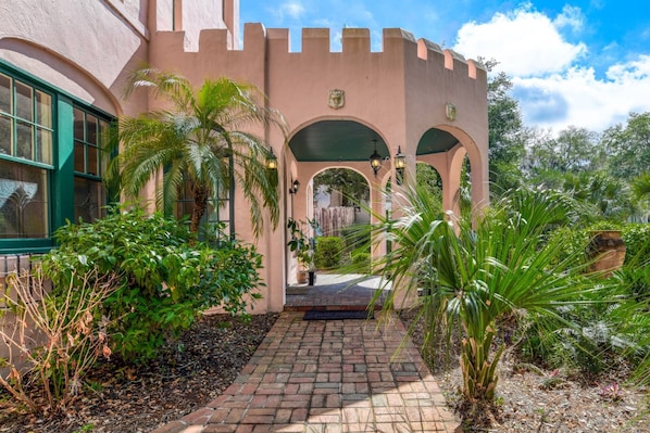 A building with a castle-like facade, arched walkways, and lush tropical plants. - Historic Home, Perfect for Special Occasions, 3 Master Suites, Steps to Sites, $300 in Free Tickets! (St. Augustine)