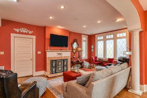 A living room with a fireplace, a television, and a large window with multiple panes. - Historic Home, Perfect for Special Occasions, 3 Master Suites, Steps to Sites, $300 in Free Tickets! (St. Augustine)