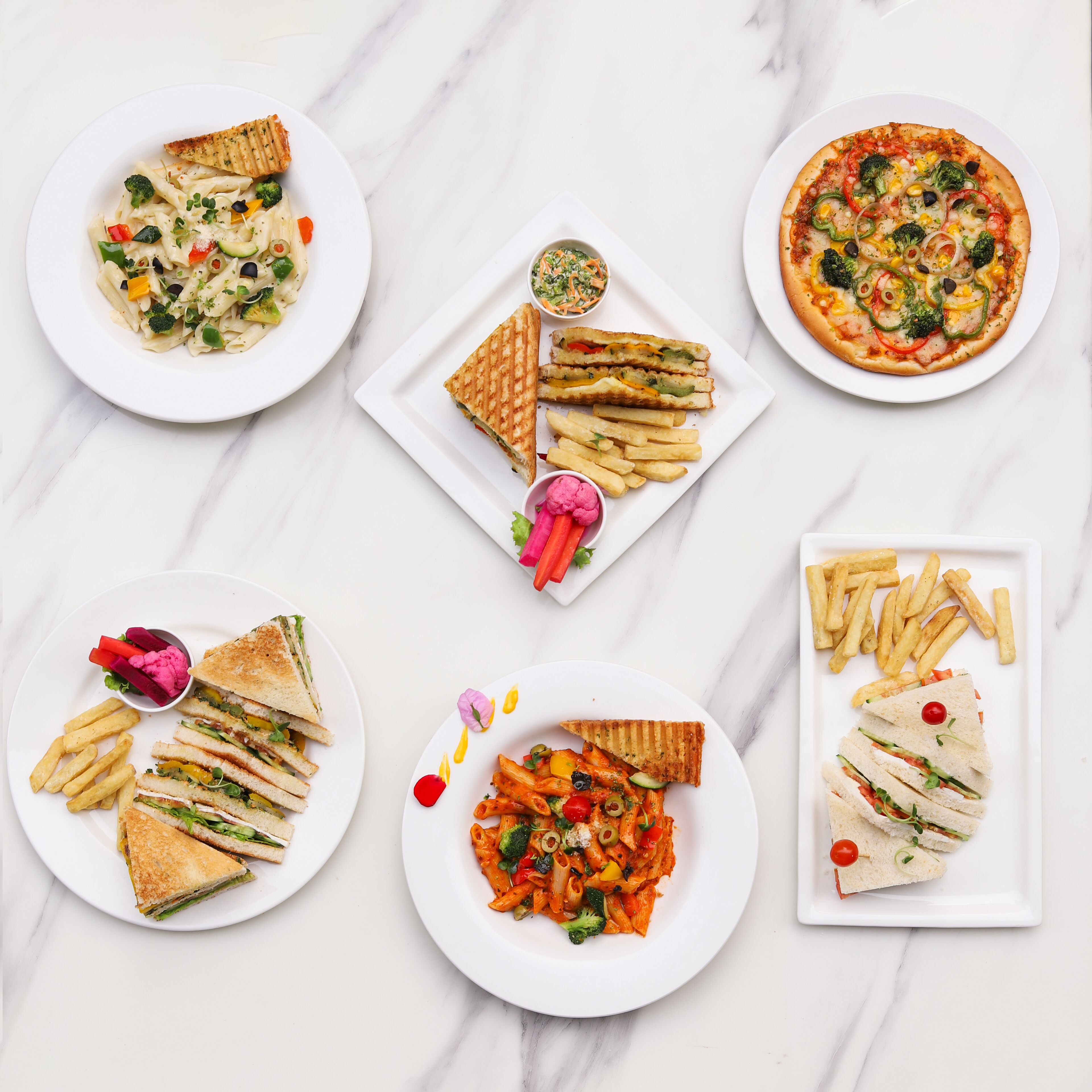 A variety of dishes including pasta, sandwiches, and a pizza, arranged on white plates.