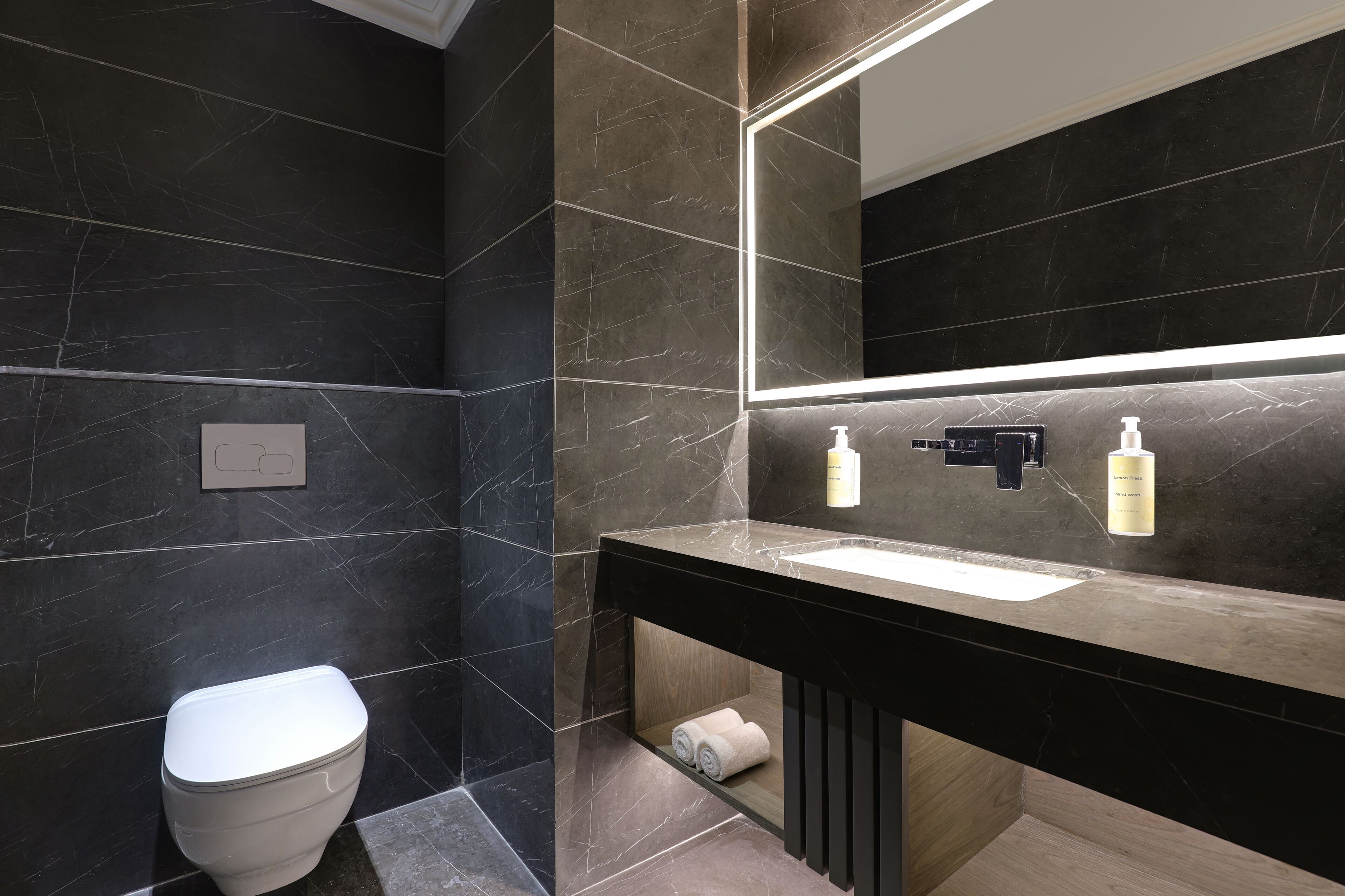 Un bany modern amb un lavabo de marbre negre, un vàter i un mirall amb il·luminació integrada.