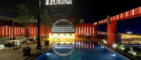 A nighttime view of a hotel pool area with a bar and seating.