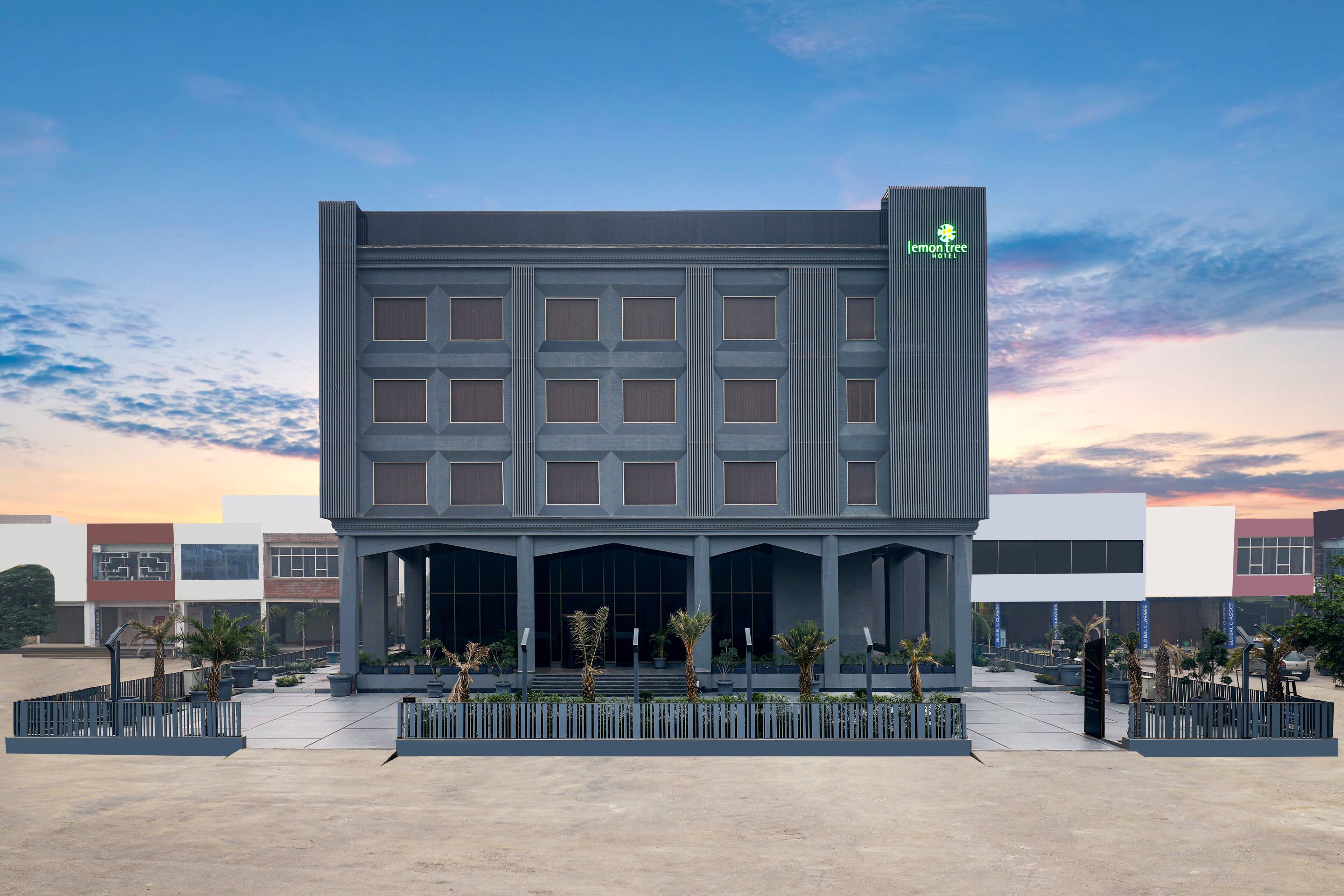 A modern hotel building with a prominent logo, large windows, and a covered entrance area.