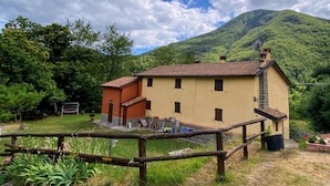 A two-story building with a red-tiled roof, a small attached structure, and a fenced yard. - Holiday Home 'La Casina Rossa Della Fornace' with Mountain View, Private Garden & Wi-Fi (Cutigliano)
