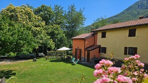 A house with a patio, a lawn, and a mountain in the background. - Holiday Home 'La Casina Rossa Della Fornace' with Mountain View, Private Garden & Wi-Fi (Cutigliano)