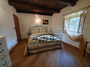 Une chambre à coucher avec un lit, un plancher en bois, un radiateur, une fenêtre avec des rideaux et une porte.