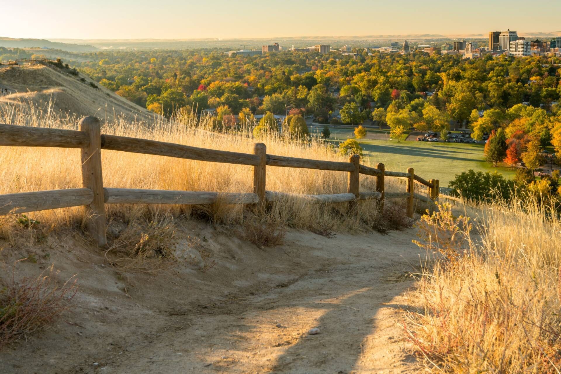 A dirt path leading to a wooden fence overlooking a cityscape with autumn foliage.