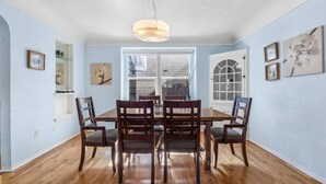 Una sala da pranzo con tavolo e sedie in legno, un lampadario a sospensione e quadri appesi alle pareti.