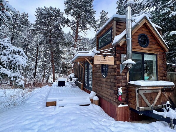 A snowshoe hare cabin with a wooden exterior, a glass door, and a sign indicating its name and species. - Snowshoe Hare Tiny Home at The Woolly Bugger Inn (Estes Park)
