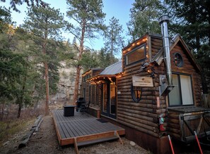 A log cabin with a deck, a chimney, and a sign indicating it is a snowshoe lodge. - Snowshoe Hare Tiny Home at The Woolly Bugger Inn (Estes Park)
