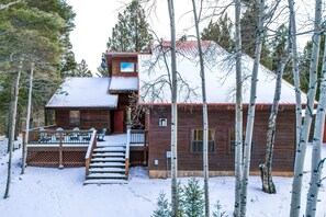 A wooden cabin with a deck and stairs leading to a second-story balcony.