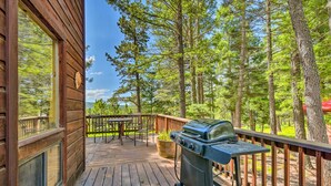 Una terraza de madera con una parrilla, mobiliario exterior y vistas a un bosque.