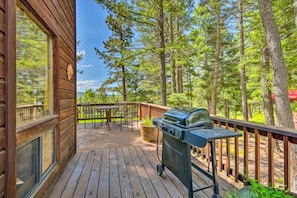 A wooden deck with a grill, outdoor furniture, and a view of a forest.