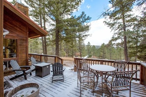 A wooden deck with outdoor furniture, including chairs and a table, overlooking a forested area.