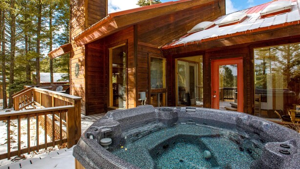 A wooden cabin with a hot tub, deck, and large windows. - Cimmaron Sky by Velo (Angel Fire)