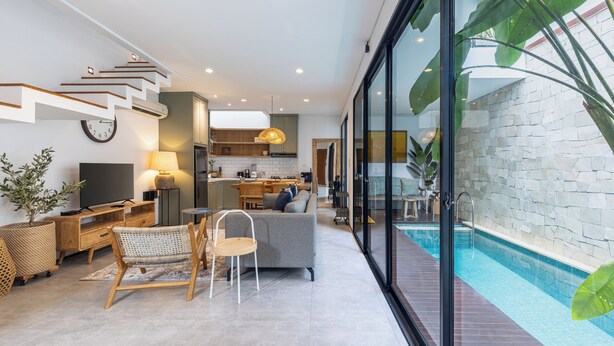 Un salon moderne avec un canapé, des fauteuils, une table basse et un téléviseur. Un escalier mène à un autre niveau.