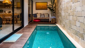 Une piscine intérieure moderne, avec des carreaux bleu clair, une terrasse en bois et un coin repas comprenant une table et des chaises.