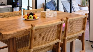 Un coin repas avec une table en bois, des chaises en osier, un panier de fruits et un luminaire suspendu en fibres tressées.