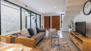 Un salon moderne comprenant un canapé, des fauteuils, un téléviseur et un coin repas avec une table mise.