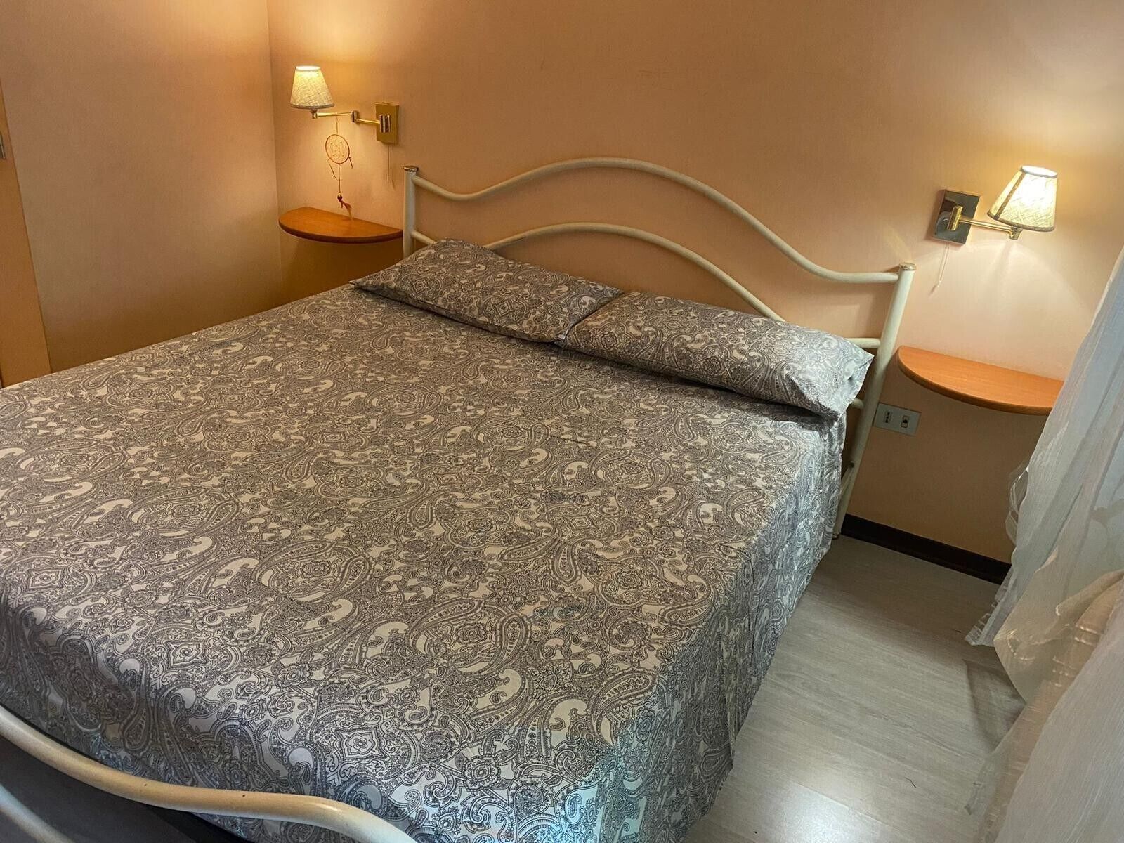 Een bed met een geborduurde sprei, een nachtkastje met een lamp, en een wandlamp.