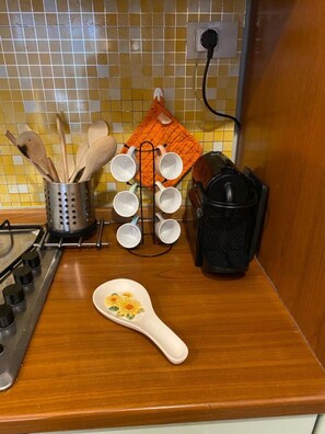 Una encimera de cocina con una estufa, una cafetera, un juego de cucharas de madera, un juego de tazas blancas y una cuchara decorativa.
