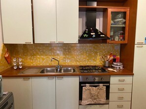 Una cocina con un lavaplatos doble, estufa y microondas. Hay armarios y salpicadero de azulejos.