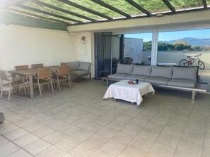 Un patio techado con una zona de comedor, un sofá y una mesa con mantel.