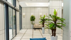 A modern lobby with a glass wall, a blue sofa, and potted plants. - Park Dedeman Almaty (Almaty)