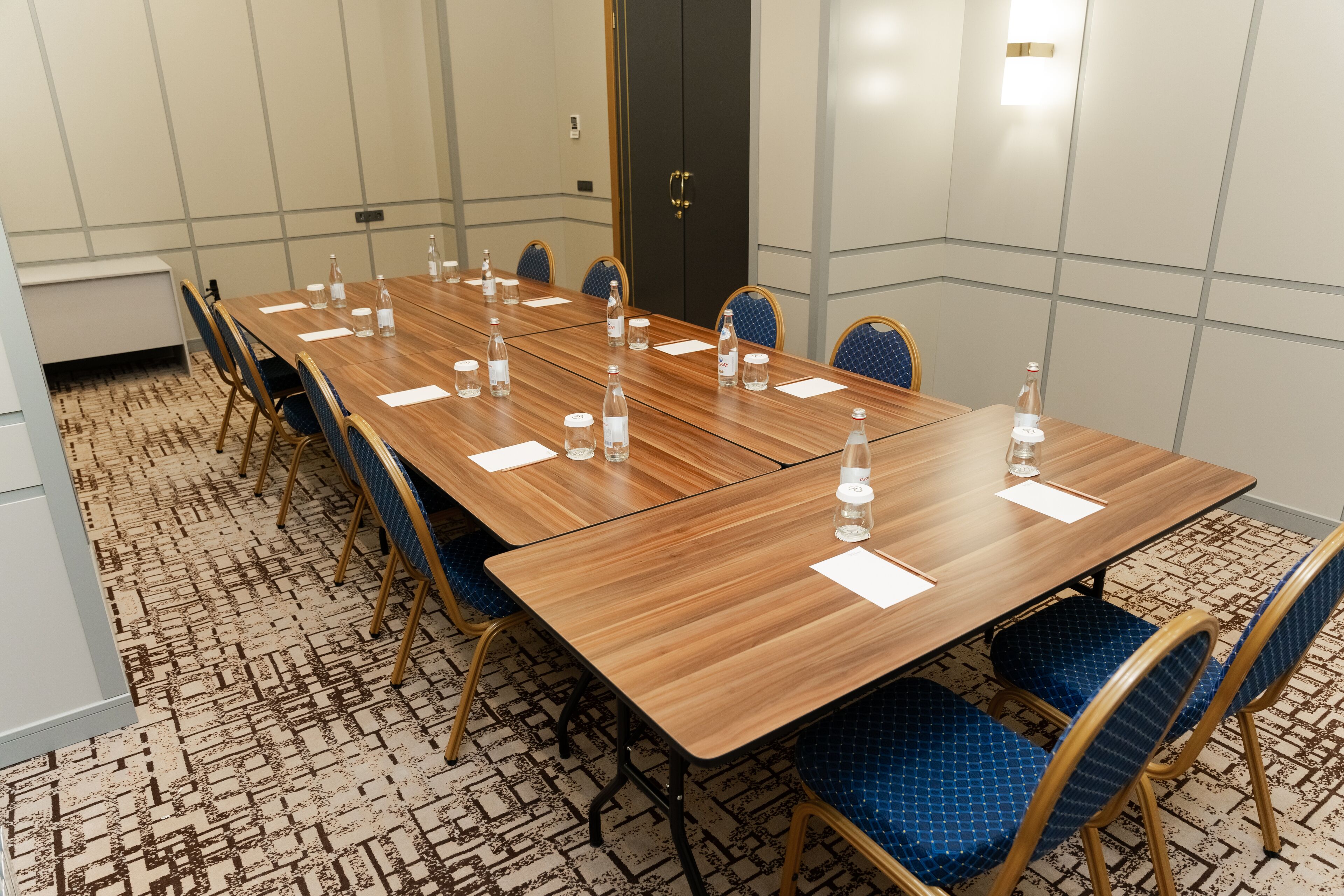 A conference room with a long wooden table, blue upholstered chairs, and water bottles on the table.