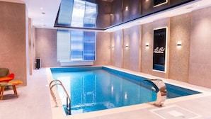 A modern indoor swimming pool with a clear view of the sky through large windows, a lounge area with a red chair, and a visible sign for 'Le Petit Wellness Club'. - Park Dedeman Almaty (Almaty)