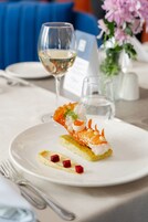 Una mesa de comedor con un plato de comida, una copa de vino blanco y un jarrón con flores.