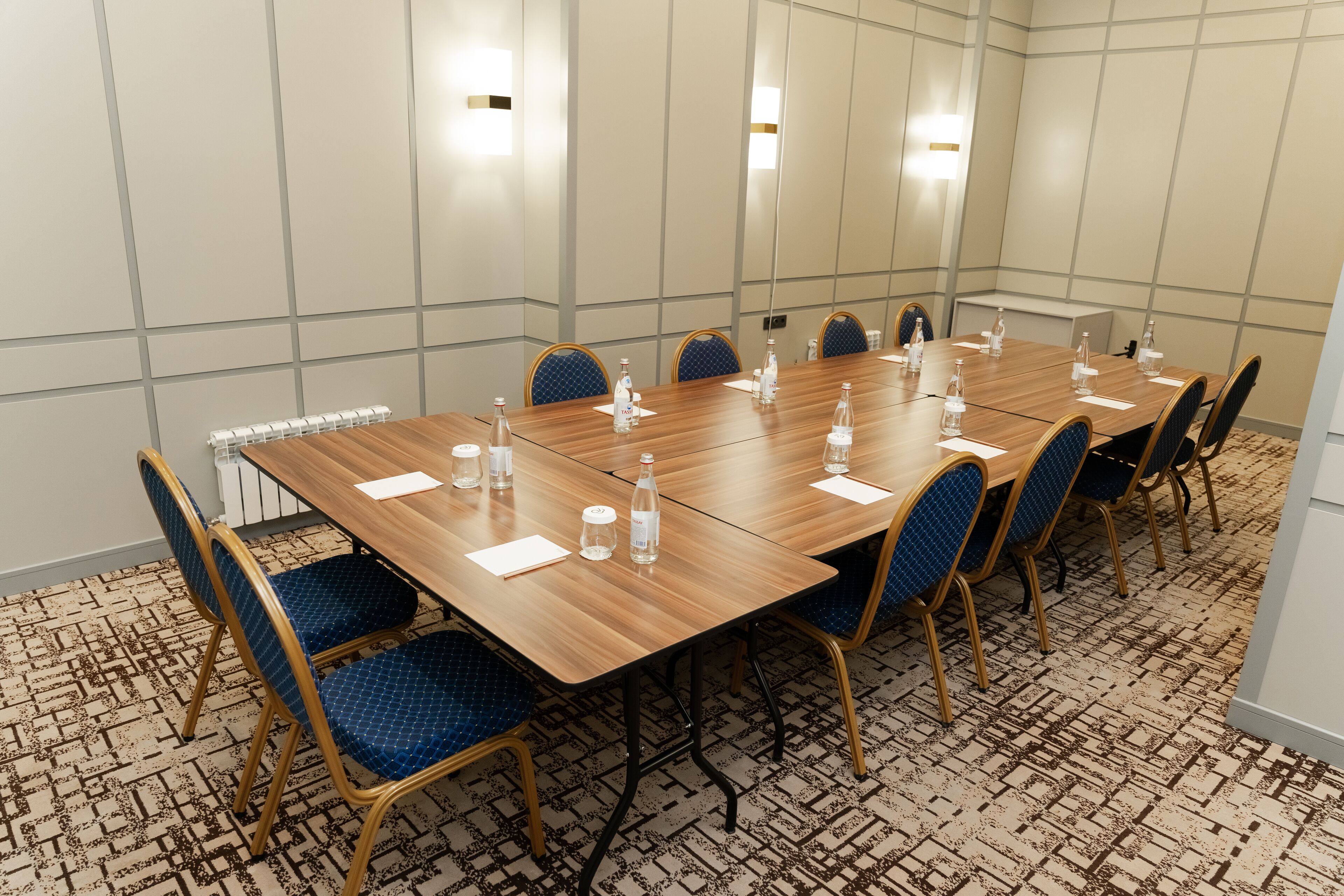 A conference room with a long wooden table, blue upholstered chairs, and a patterned carpet.