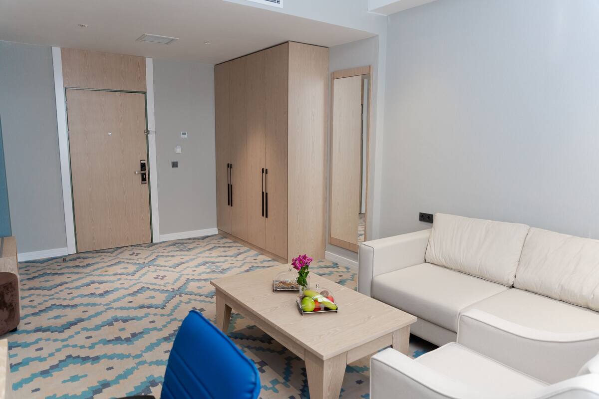 A modern room with a beige sofa, a wooden table with a vase and fruit, a blue chair, and a large wardrobe.
