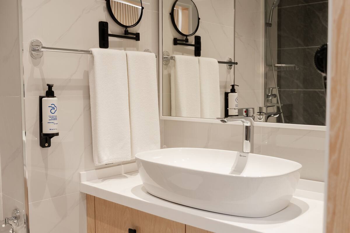 A modern bathroom with a large mirror, a white sink, and a shower.